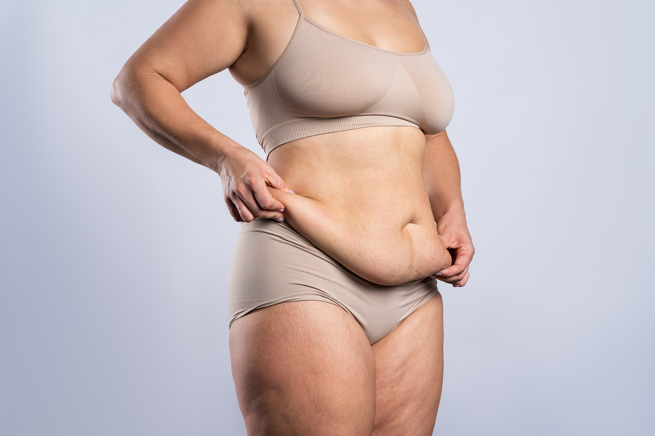 woman holding stubborn belly fat and hanging skin